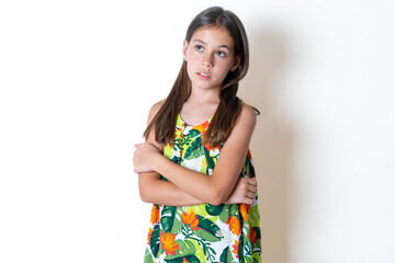 Charming thoughtful Beautiful kid girl wearing floral dress stands with arms folded concentrated...