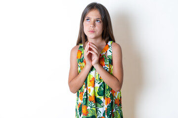 Beautiful kid girl wearing floral dress steepled fingers and looks mysterious aside has great evil...