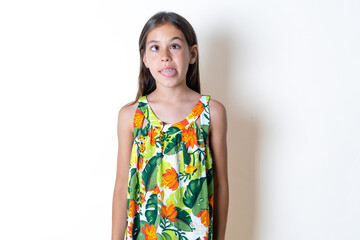 Funny Beautiful kid girl wearing floral dress makes grimace and crosses eyes plays fool has fun...