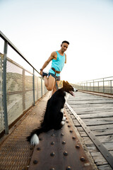 An adult man with an amputated arm is stretching his leg with a harness with a dog on an outdoor bridge. Canicross concept, running with a border collie.Sports activities with animals.