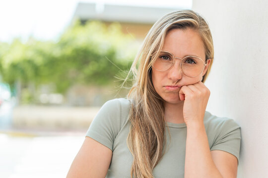 Young blonde woman at outdoors With glasses and with sad expression
