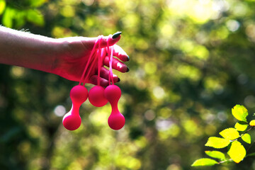 Woman's hand holds pink Kegel balls, Ben Wa balls against a background of green bushes in the forest. Vaginal balls in a woman's hand. Sex toys Geisha balls. Sex shop - obrazy, fototapety, plakaty