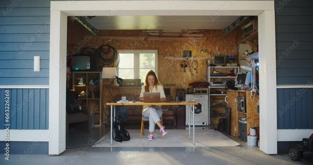 Poster hispanic female software engineer coding on laptop computer in garage at home. focused young woman w