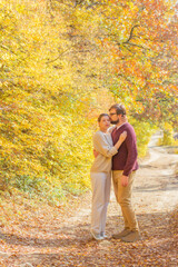 Beautiful couple hugs a man kisses on the forehead of a woman in cozy knitted sweaters in the autumn forest. Concept: vacation trip weekend in the forest autumn among trees colored seasonal leaves 