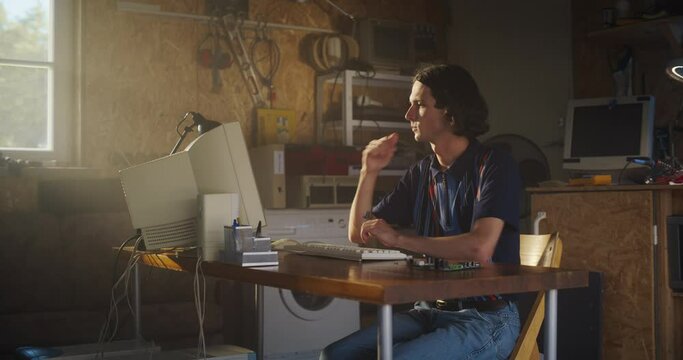 Caucasian Male Software Engineer Programming On Old Desktop Computer In Retro Garage With Random Appliances. Man Starting an Innovative Fintech Startup Company In Nineties. Nostalgia Concept.
