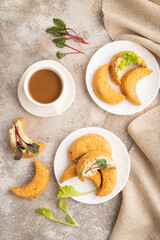 Homemade salted crescent-shaped cheese cookies, cup of coffee on brown concrete. top view.