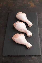 Raw chicken legs on a black slate cutting board on a black concrete background. Side view.