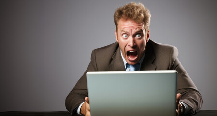Hombre rubio de 25-35 años, sorprendido y angustiado frente a un ordenador, vestido con traje y corbata, expresando pánico. Fondo gris. - obrazy, fototapety, plakaty