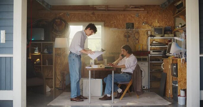 Two Caucasian Male Stock Traders Working In Retro Garage, Using Old Desktop Computer With Candlestick Chart And Landline Phone To Pitch A Public Company To Investors. Partners Starting Hedge Fund.