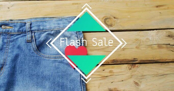 Animation of flash sale text over denim trousers on wooden background