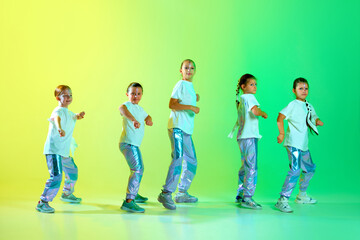 Cool girls in fashion outfit with bright glittered makeup performing new dance tricks, synchronous movements over gradient yellow-green background.