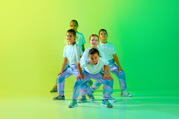 Team of smiling attractive girls children dressed in fashion, stylish outfit dancing in choreography class isolated on green-yellow gradient background. - obrazy, fototapety, plakaty