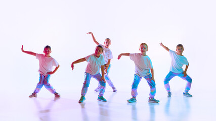 Fototapeta na wymiar Group of girls wearing sporty style clothes with trendy, creative hairstyle dancing synchronous choreography class over gradient background in neon light.