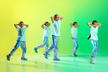 Cool little girls in fashion outfit with bright glitter makeup performing new dance moves synchronous over gradient yellow-green background.