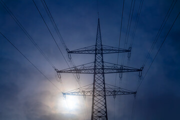 Steel structure of a high voltage pylon with wires, insulators, blue sky and low sun seen from frog...
