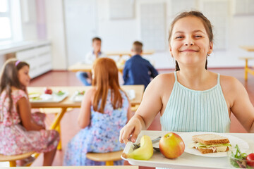 Happy girl holding healthy food tray in school cafeteria