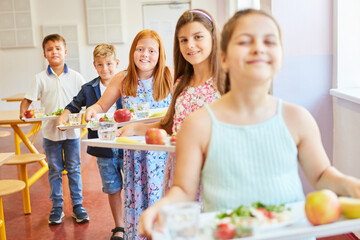 Smiling kids with food trays standing in line at school cafe
