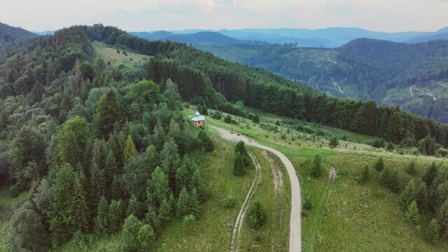 the camera moves to the right, flying around the church on top of the mountain, and revealing an amazing mountain landscape. Ukrainian Carpathians, evening, summer, 4K