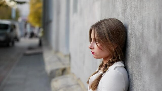 An upset girl sits near the wall of a building and looks at the camera.