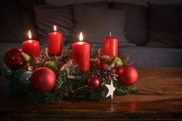 Advent wreath with three burning red candles and Christmas decoration on a wooden table in front of...