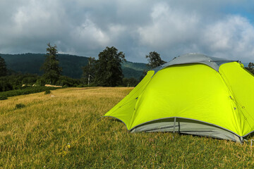 A relaxing holiday in nature with camping equipment, a green tent and the necessary materials in an empty area full of greenery and mountains.