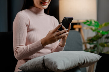 Asian woman is in the living room and uses social media on a smartphone. Female company employee on vacation. Using vacation time and free time to relax at home. Weekend vacation day doing activities.