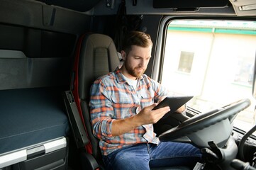 Man truck driver sitting behind wheel of car and holding digital tablet in his hands - obrazy, fototapety, plakaty