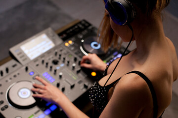 Top view of female disc jockey mixing tracks on professional sound mixer, playing music during night at nightclub. Attractive young dj woman.