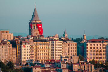 Galata Tower is located in the Beyoğlu district of Istanbul. As the sun sets, its lights reflect on the Galata tower and buildings. The Turkish flag hanging on the Galata Tower. Istanbul, Turkey. - obrazy, fototapety, plakaty