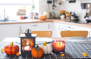 Decor of white classic kitchen with pumpkins, garlands, latern for Halloween and harvest with figurine of house. Autumn mood in home interior, modern loft style. real estate, insurance, mortgage