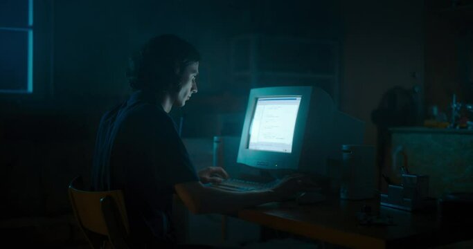 Caucasian Male Web Designer Using Old Desktop Computer In Retro Garage Late At Night. Focused Internet Enthusiast Writing Code At Home. Programming Successful Online Forum Website In Nineties.