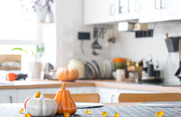 Fototapeta na wymiar Decor of white classic kitchen with pumpkins, garlands, latern for Halloween and harvest with figurine of house. Autumn mood in home interior, modern loft style. real estate, insurance, mortgage