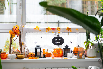 Festive decor of the house on the windowsill for Halloween in interior with homemade potted plants- pumpkins, Jack o lanterns, skulls, skeletons, candles and garland - cozy and terrible mood