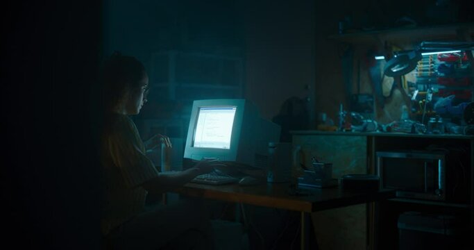 Hispanic Female Programmer Using Old Desktop Computer In Retro Garage Late At Night. Evil Hacker Searching For Software Vulnerabilities, Doing DDOS Attack, Coding Trojan Horse Programs, Stealing Data.
