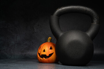 Kettlebell and Halloween pumpkin, spooky Jack-o'-lantern decoration. Healthy fitness composition with copy space. Gym workout, sport training concept. Staying in shape during autumn fall season.