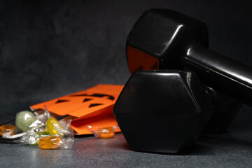 Gym dumbbells and Halloween treat bag filled with candies sweets. Staying in shape during autumn...