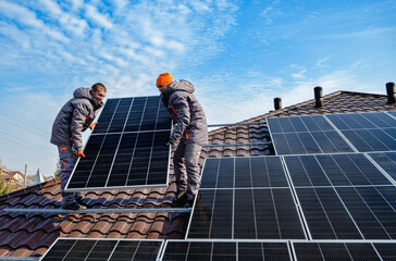 Men technicians carrying photovoltaic solar moduls on roof of house. Engineers installing solar...