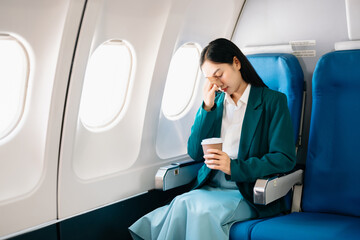 Photo of a frustrated woman sitting on an airplane with her head in her hands. Asian woman sitting in a seat. - obrazy, fototapety, plakaty