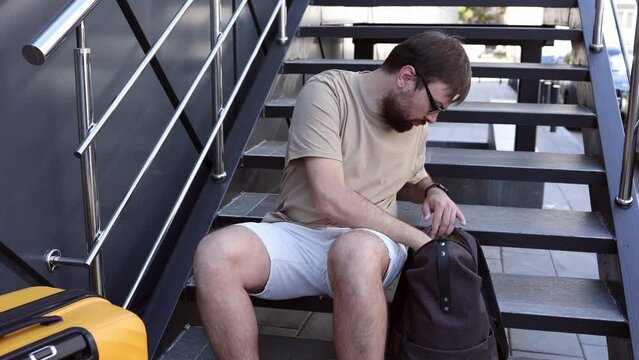 Man forgot or lost his documents and boarding pass for the plane. Travel theft. A frustrated man holds his head. Orange suitcase, backpack. Search for tickets in your backpack. Problems in travel