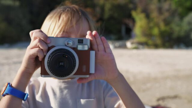 A young boy is using an instant camera to take a photograph at the beach.