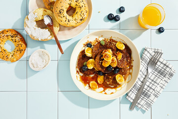 Sweet breakfast with banana pancakes and freshly baked bagels. Top view. Tiled background, hard light.