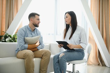 Psychologist talking with patient on therapy session. Depressed man speaking to a therapist while she is taking notes