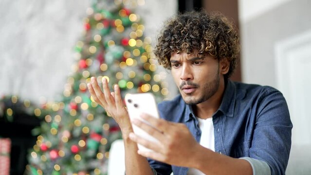 Close up. Frustrated stressed handsome man reads bad news on a smartphone while sitting at home during winter New Year Christmas holidays. Worried upset male is sad while reviewing negative message