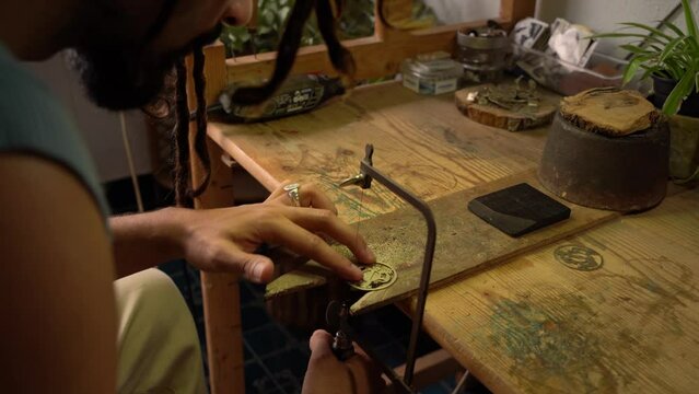 Young craftsman trimming workpiece with a hacksaw on a workbench. Goldsmith workshop. Copy space on the right