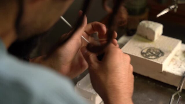 Close up of the hands of a craftsman cutting pieces with shears. Goldsmith workshop, workbench.