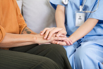 Up close, an elderly female patient holds hands with a nurse who comes to take care of her and help to encourage each other.
