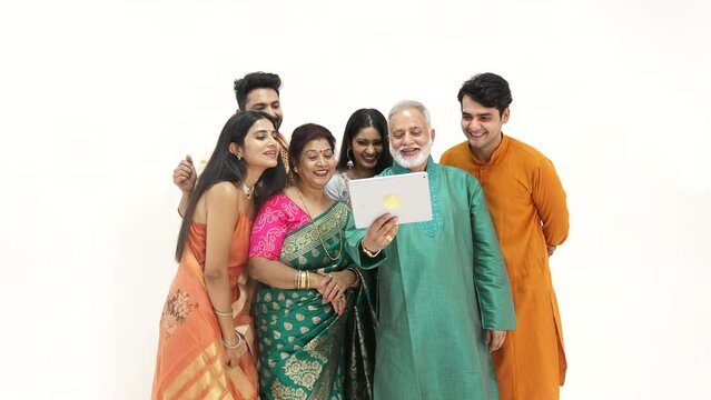 Cheerful Indian family  waving their hands while talking on a video call on ipad- a celebration time. Happy family celebrating the festival of Diwali together - festive season, a Hindu festival