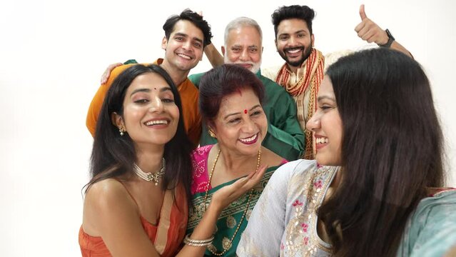 Happy smiling Hindu ethnic Indian family members in traditional attire posing to take or click a selfie picture or photo together using a mobile phone during Diwali festival season.