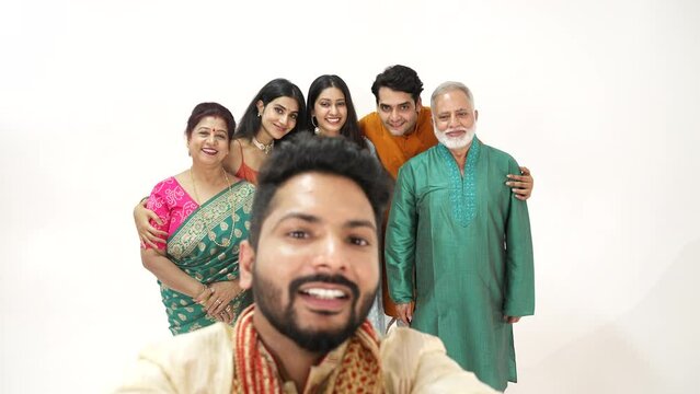 smiling Hindu ethnic Indian family members in traditional attire posing to take or click a selfie picture or photo together using a mobile phone during Diwali festival season.
