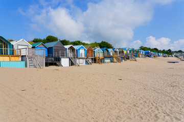 Multi coloured wooden beach huts line the back of Abersoch beach in Wales on a summer afternoon.